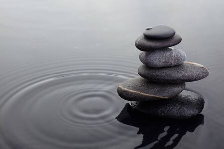 Zen stones in balanced pile in water on rippled water surface.の写真素材