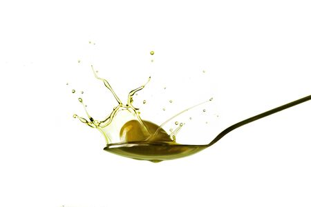 droplets obtained from an olive that falls on a spoon full of olive oil isolated on whiteの写真素材