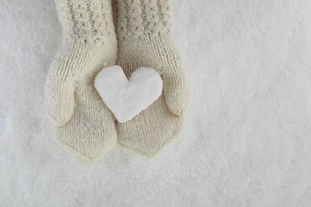 Snow Heart in Hands with Mittens on white snow backgroundの写真素材