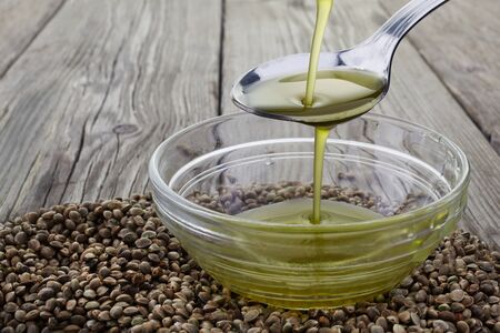 Pouring hemp oil into glass bowl and hemp seeds on wooden backgroundの写真素材