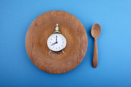 Eight hour feeding window concept or breakfast time with clock on plate and wooden spoon.
