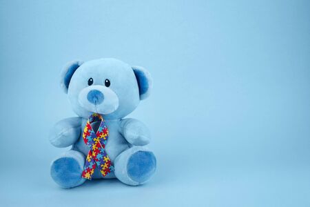 World Autism Awareness, concept with teddy bear holding puzzle or jigsaw pattern ribbon on blue backgroundの写真素材
