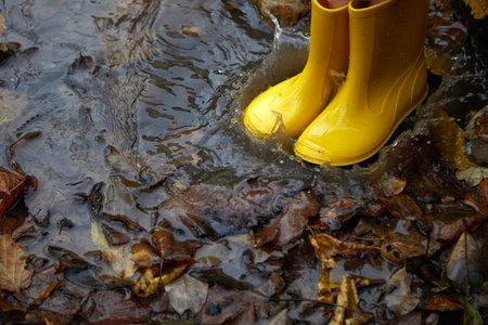 Feet of child in yellow rubber boots jumping in puddle at the autumn day.