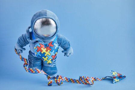 Autism awareness background. Blue plush astronaut toy with puzzle heart, autism symbol, on blue...
