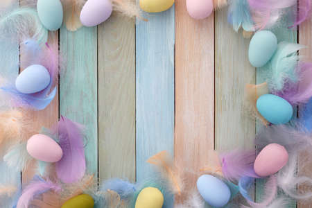 Happy easter concept. Frame with colorful Easter eggs and feathers on wooden background. Flat lay.の写真素材