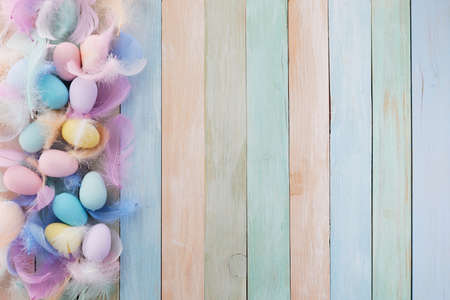 Happy easter concept. Frame with colorful Easter eggs and feathers on wooden background. Flat lay.の写真素材