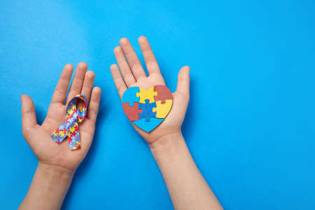 Adult and autistic boy hands holding puzzle heart shape and ribbon. Autism spectrum disorder family support concept. World Autism Awareness Dayの写真素材
