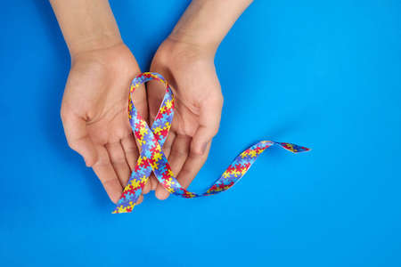 World Autism awareness day. Autistic boy hands holding puzzle pattern ribbon on blue backgroundの写真素材