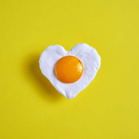 Heart shaped fried egg on yellow background, for the world egg day.の写真素材