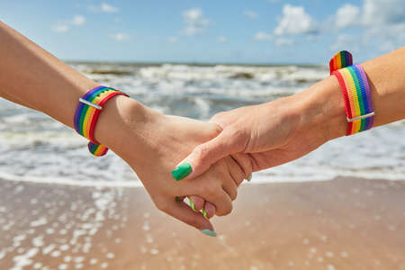 Two caucasian womens holding hands with a rainbow-patterned wristban on their wrists.の写真素材