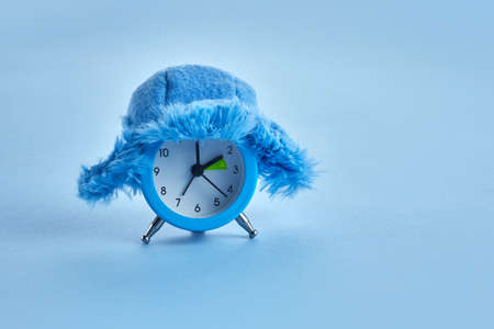Clock changing from summer to winter time. Alarm clock with winter hatの写真素材