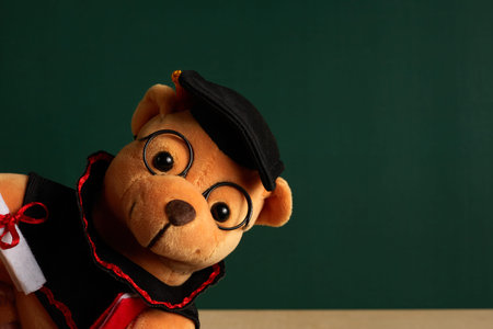 Teddy bear with graduation hat and diploma in front of green chalkboard. Graduation conceptの写真素材