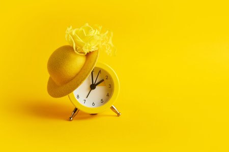 Daylight saving time. Spring forward. Alarm clock with hat on yellow backgroundの写真素材