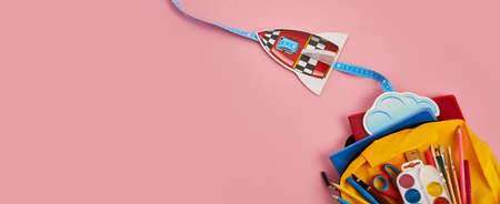School backpack with colorful school supplies and rocket on pink backgroundの写真素材