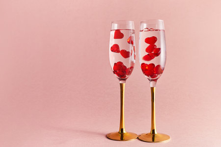 Happy Valentines Day. Two glasses of champagne wine with red hearts in them. Pink background.の写真素材
