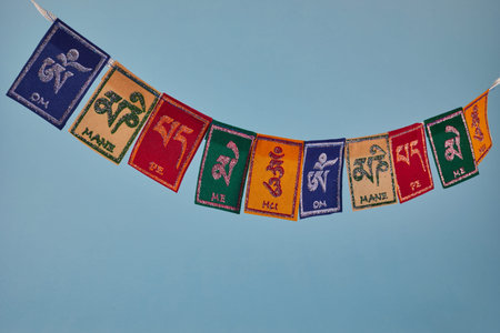 Tibetan Buddhist flags against blue background. Text on flags Om mani padme hum meaning The jewel is...