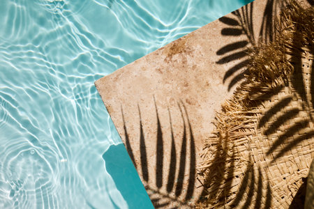 Top view of a straw hat casting a palm shadow on a poolside, creating a tranquil summer vibe.の写真素材
