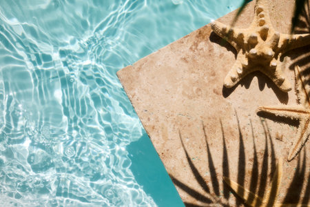 A starfish on a stone ledge casting a shadow over sparkling pool water.の写真素材