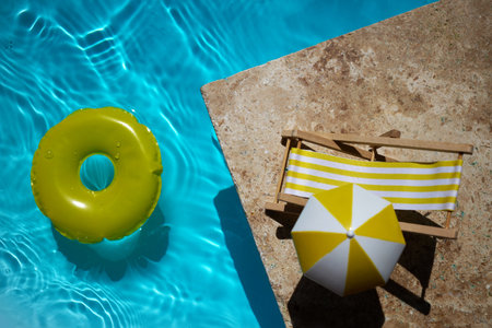 A bright yellow float and mini deck chair beside a pool with clear blue water.の写真素材