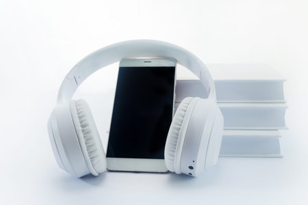 White headphones around a smartphone, with a stack of books in the background.
