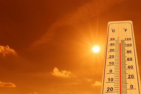 A thermometer indicating high temperatures under an intense, bright orange sky with blazing sunlight.の写真素材
