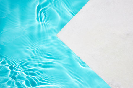 Minimalist poolside design with turquoise water and white platform under bright sunlight.の写真素材