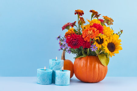 Autumn Floral Display. A vibrant bouquet in a pumpkin vase with blue candlesの写真素材