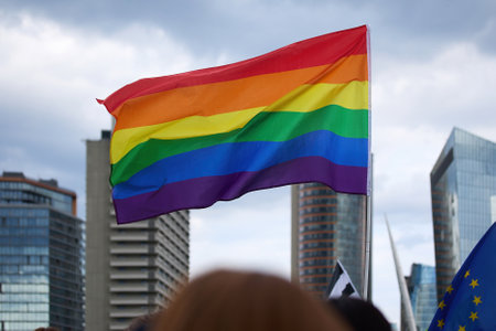 Pride Flag in Urban Setting. A vibrant rainbow flag waves against a city skyline,の写真素材