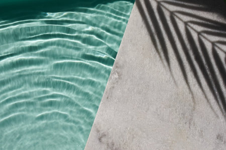 Poolside Serenity. Rippling water by sunlit poolside with palm shadows.