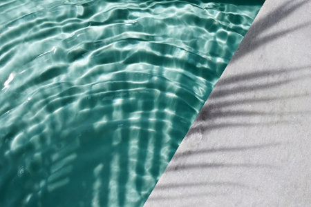 Poolside Serenity. Rippling water by sunlit poolside with palm shadows.