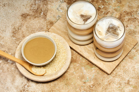 Creamy Tahini Latte Coffee and with tahini cream bowl and sesame seeds on a marble travertineの写真素材