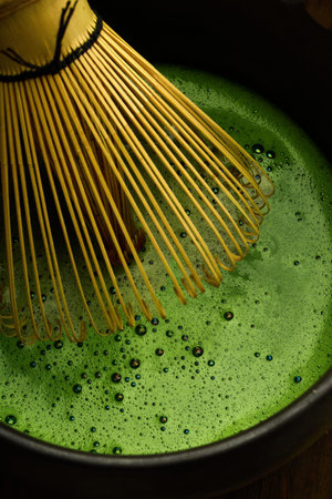 Matcha Whisking. A bamboo whisk stirs vibrant green matcha with bubbles.