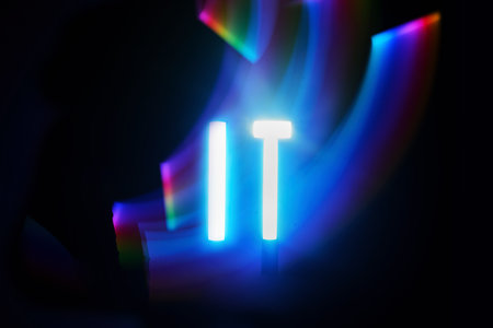 Illuminated IT. Neon IT text with vibrant light trails in the darkの写真素材