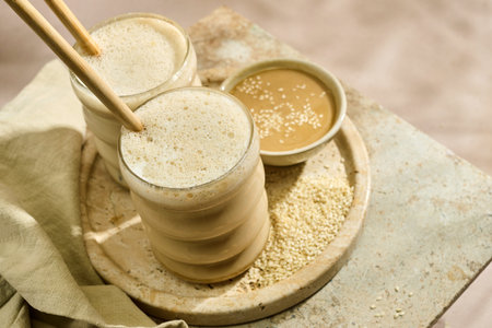 Sesame Tahini Latte Delight. Creamy sesame paste and iced tahini lattes on rustic travertine surface.の写真素材