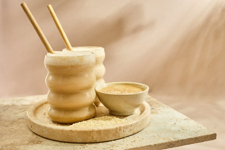 Sesame Tahini Latte Delight. Creamy sesame paste and iced tahini lattes on rustic travertine...