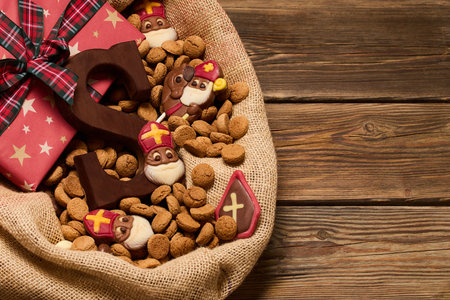 Festive Treats and Gifts. Sinterklaas chocolates and cookies in a burlap sack on a wooden table.の写真素材