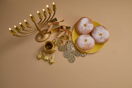 Hanukkah Celebration Setup. A menorah, dreidels, gift boxes, and donuts on a beige background