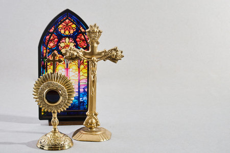 Gold monstrance, crucifix, and stained glass window on a light background