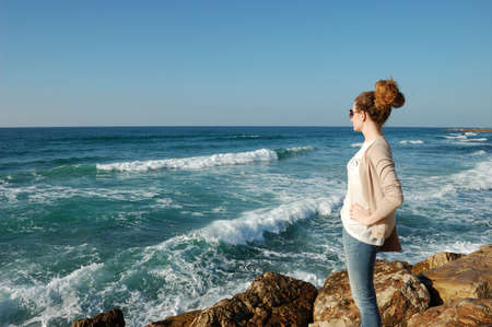 youngyoung curly-haired girl, looking into the distance of the sea, in jeans, glasses, surf stones on vacation by the sea, tourism, blue sea curly-haired girl, looking into the distance of the sea, in jeans, glasses,の写真素材