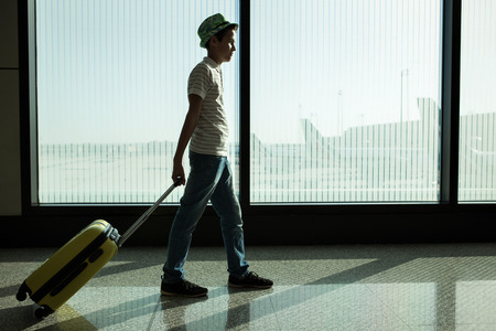 little boy with suitcase waiting in the airportの写真素材