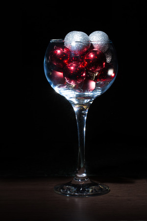 Wine glass filled with Christmas balls. On a black background.の写真素材