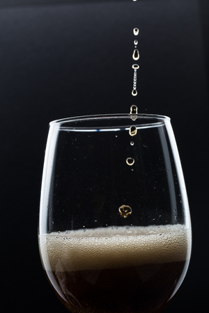 Glass of pouring fizzy drink with ice on a black backgroundの写真素材