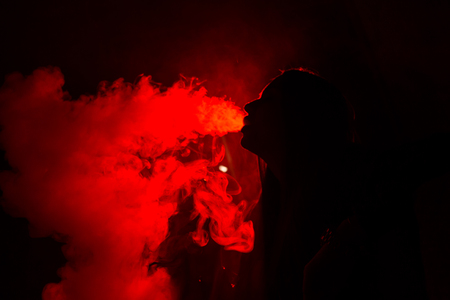 Girl model smokes vape in red light.の写真素材