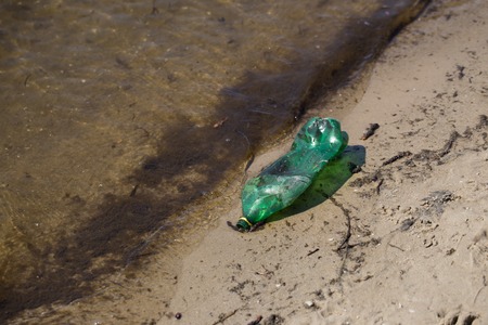 Plastic bottle of green color in a pond on a muddy beachの写真素材