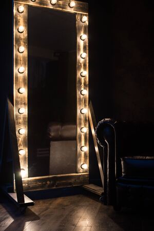 Antique mirror with incandescent lamps and a dark leather sofaの写真素材