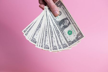 A bundle of dollar bills in a male hand on a pink background.の写真素材