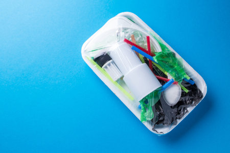 Set of plastic waste in a packed tray on a blue isolated background. The problem of ecology and...