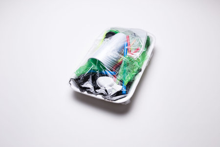 Male hand holds a tray with plastic waste on a white isolated background. The problem of ecology and...