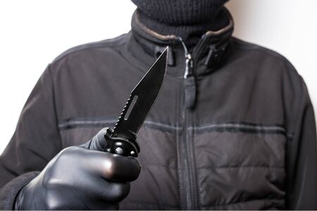 A man in a black jacket with a knife on a white background. Robbery or crime with a knife.の写真素材
