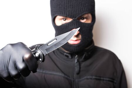 A man in a black jacket with a knife on a white background. Robbery or crime with a knife.の写真素材